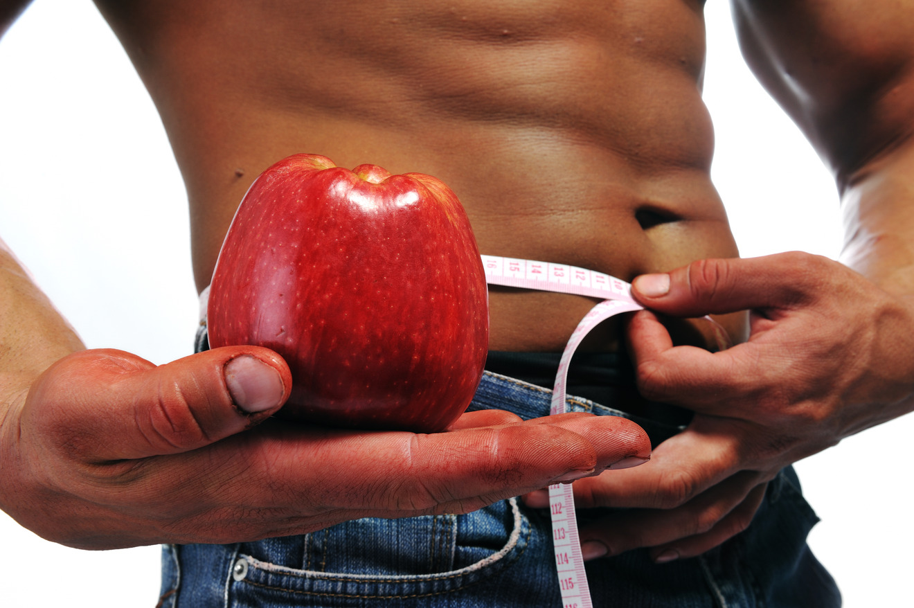 a man holding a tape measure around his waist with one hand and an apple with the other hand