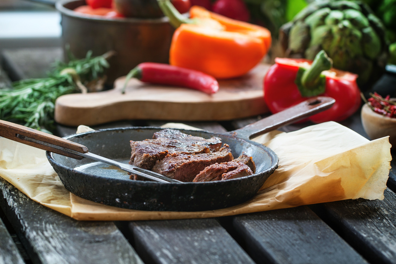 meat on a pan with vegetables in the background