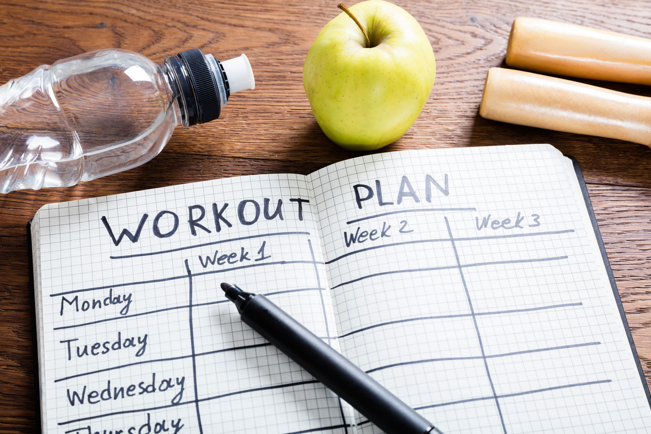 Workout notebook, apple, and water bottle on table