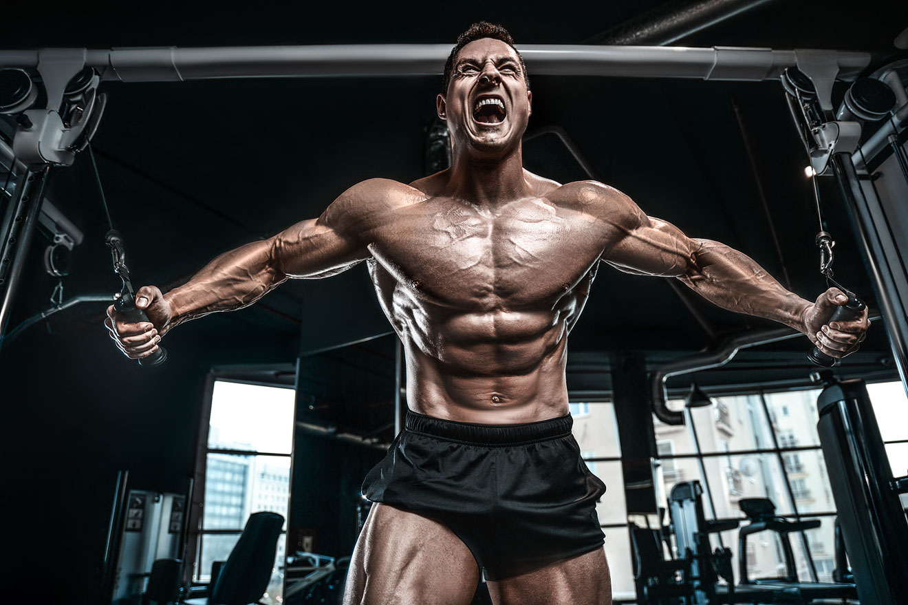 shirtless man in gym straining to do cable fly exercise