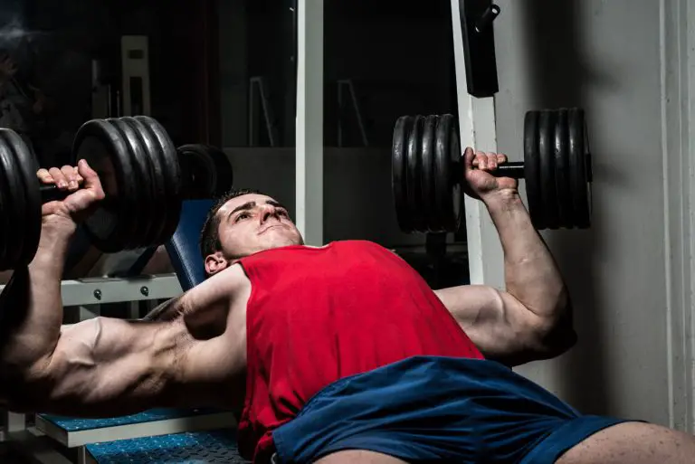 Man in vest doing dumbell dench press with heavy weights