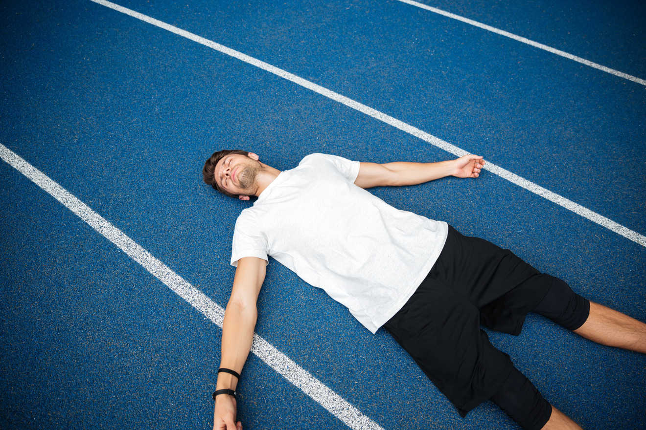 tired male athlete resting after running on racetrack