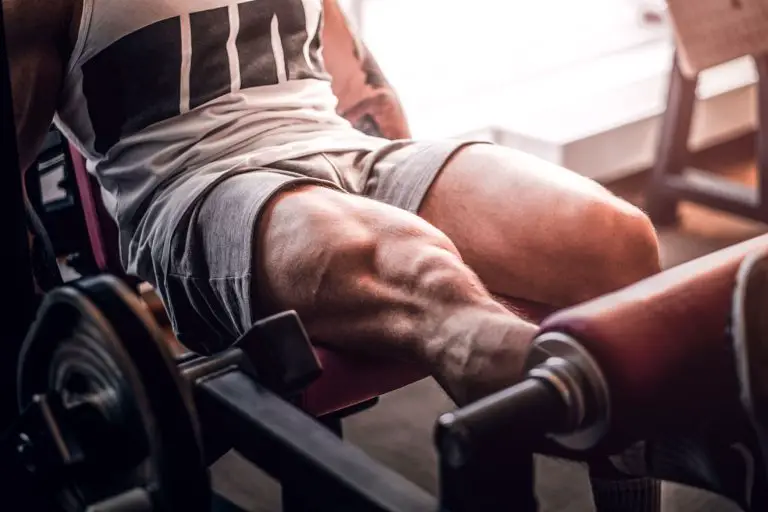 Man in gym doing single-leg knee extension exercise, with muscles bulging