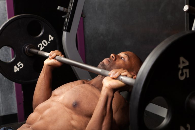 bare-chested black man doing incline barbell bench press in gym