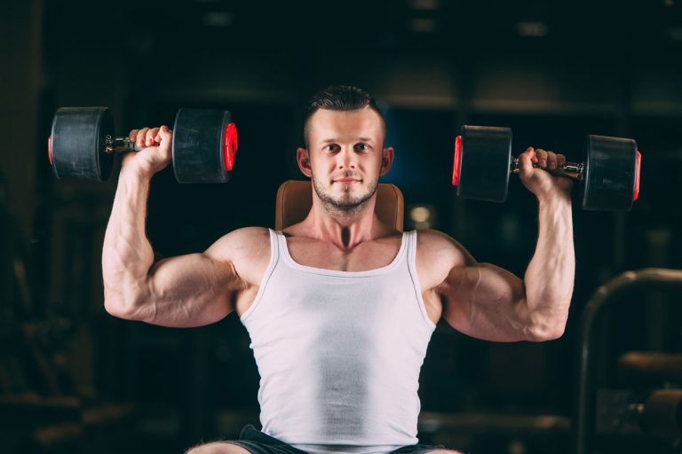 White man in gym doing dumbbell shoulder press exercise