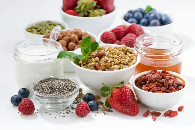 Assorted healthy fruits, berries, nuts, and cereals laid out on a white table