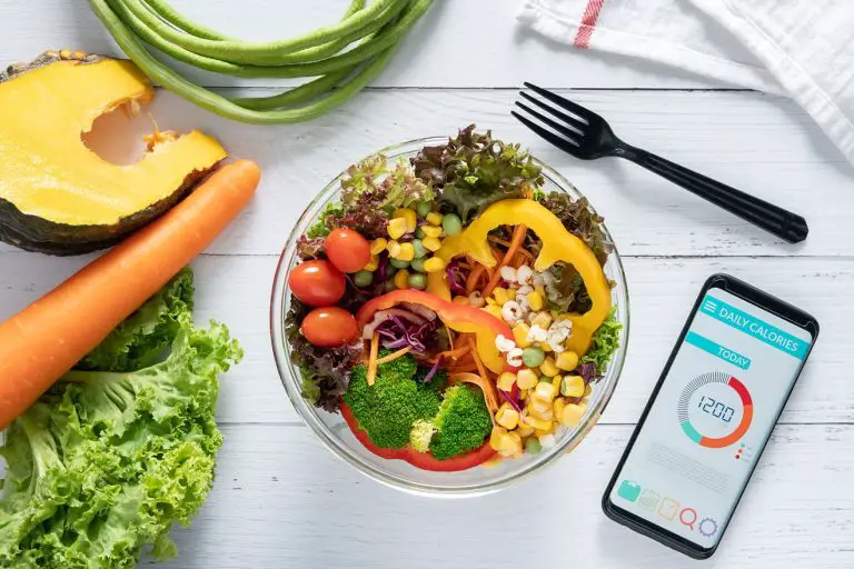 Plate of healthy food, fork, and cell phone with calorie-counting app on a dinner table