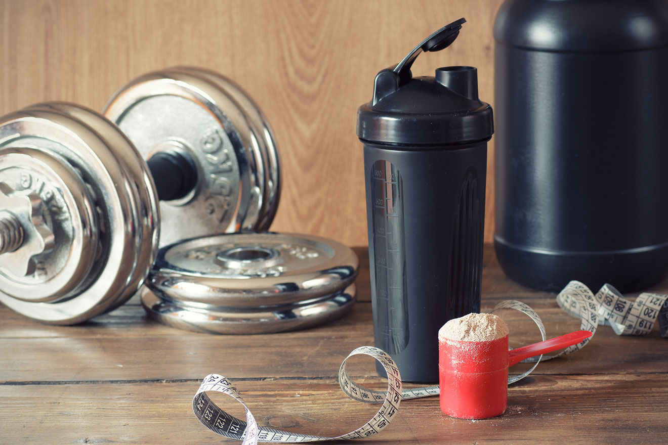 dumbbell, tape measure, drink, and supplements on a table